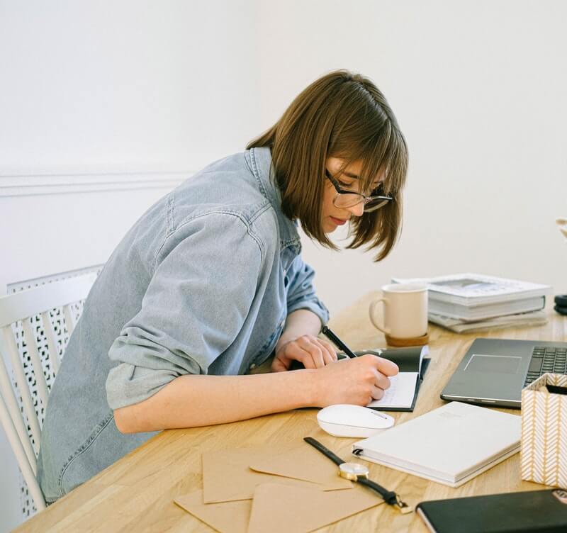 A woman writing details for her small business on a wooden desk
